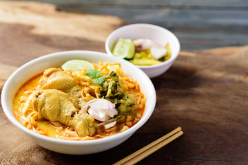 Northern Thai food (Khao Soi), spicy curry noodles soup with coconut milk and chicken in a bowl on wooden background