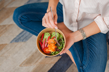 Girl holds a paper plate with healthy food sitting on the floor. Home delivery food. Healthy eating concept.