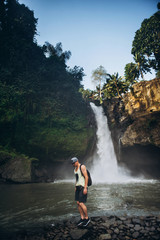 young guy in a yellow T-shirt and shorts on the background of a waterfall in Asia on the island of Bali