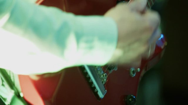 Man caucasian guitarist hand plays fingers on electric guitar fretboard, yanks strings on stage at party, multi-colored disco light around