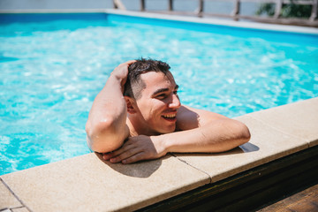 A young brunette European-looking guy peeps from the pool on a sunny day