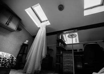 black and white photo, a beautiful wedding dress hanging under a skylight in a chic interior