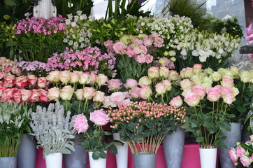 Fototapeta na wymiar Mixed of summer flowers displayed in front of a flower shop, delicate white, pink and red roses and other decorative indoor plants photographed with soft focus 