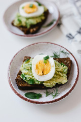 Avocado toast on black bread with seeds with egg and herbs on a plate. Guacamole