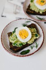 Avocado toast on black bread with seeds with egg and herbs on a plate. Guacamole