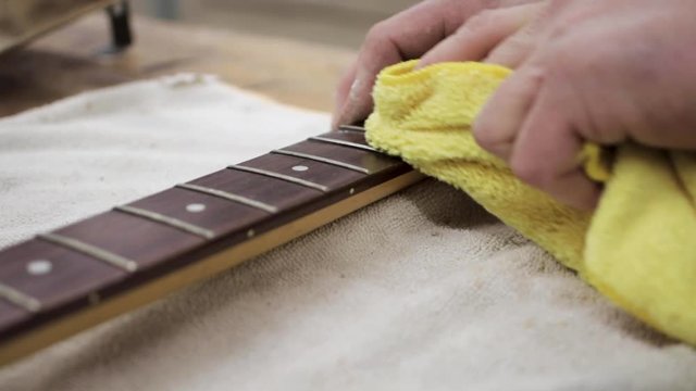 Man cleaning the fretboard of a guitar that he is refinishing.