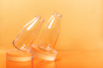 Glass bottles milk packaging on clear sphere shape stands on orange background. Creative minimalist still life