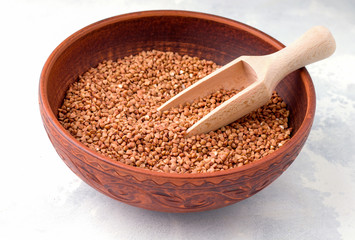 Buckwheat in a brown clay bowl on a light gray concrete background