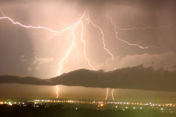 the crash of thunder and lightning over the city among the clouds through the night sky over the...