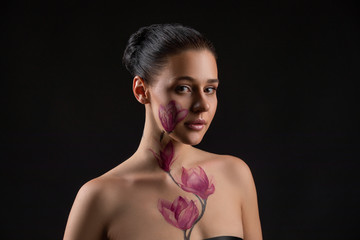 Cute girl with dark hair, body art paintings on neckline and face, naked shoulders, painting magnolia flowers, make up model