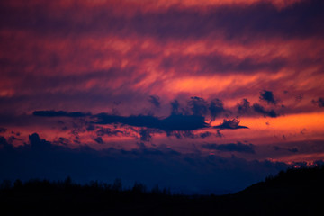 Bright red sunset among blue clouds. Mystical silhouettes in clouds