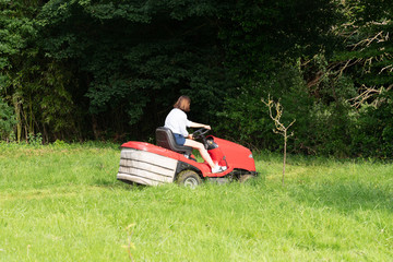 woman gardener with red modern tractor in field garden job driving a lawn mower