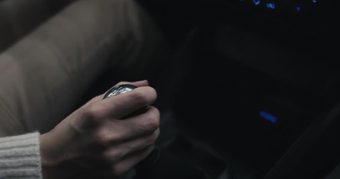 Woman's hand shift gears driving a car traveling on a regional road trip at night close up