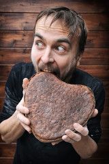 man try greedily bites off piece of rye rough bread in shape of heart and look around, concept of...