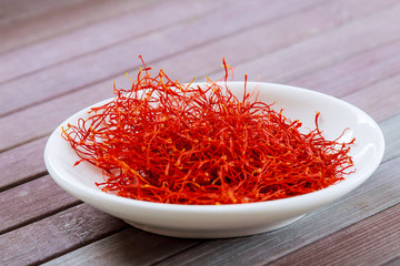 Dry Saffron Spice on a white Plate on Wooden Background.