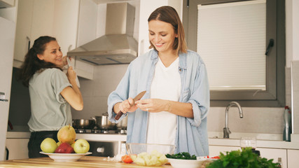 Two young beautiful women girlfriends lesbian couple cook at home in the kitchen cuddling and...