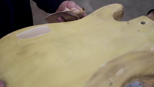 Man sanding the body of a telecaster guitar that he is refinishing.
