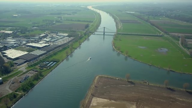 Aerial drone shot of tilting up over the canal revealing boat, bridge, and road on the flat landscape of the Netherlands.