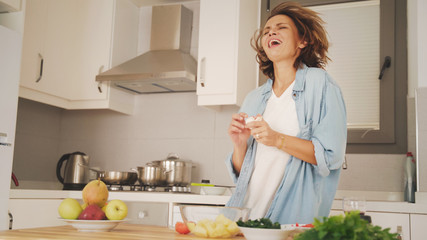 Young attractive woman joyfully sings in the kitchen cooking dinner, positive healthy eating lifestyle and hobby cooking