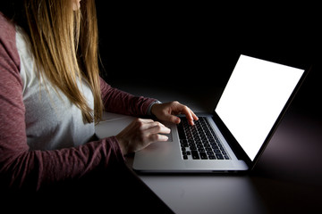 The young woman sitting in the dark living room and working with laptop