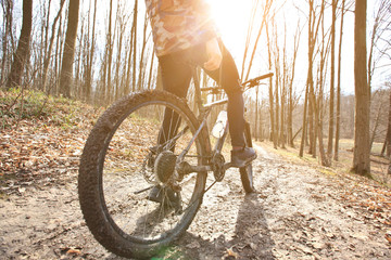 The cyclist is riding on mountain bike on dirt trail in forest in the early spring