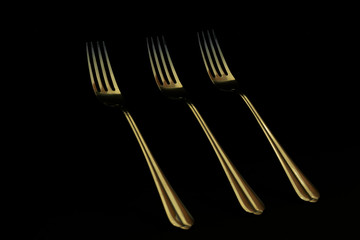Three golden forks on a black background. Abstraction and minimalism. Light and shadow
