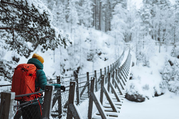 Woman crossing a suspension bridge in a snowy forest, Finland - obrazy, fototapety, plakaty