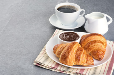 Croissants, chocolate butter, coffee and milk on a gray background.