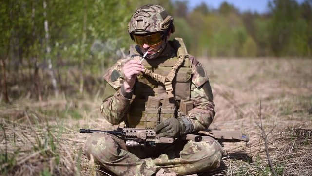 A warrior or military soldier dressed in camouflage Lights a match and lights a cigarette and smokes