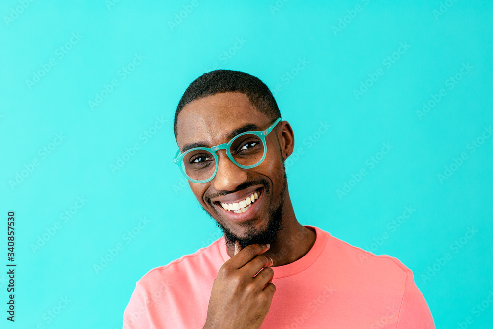 Wall mural portrait of a happy young man with glasses smiling, thinking and looking at camera with hand on chin