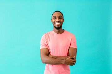 Portrait of a happy young man smiling with arms crossed, against blue studio background