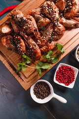 Appetizing fried prawns on a wooden tray among seasonings. Studio photography of food in the cooking industry, dark background