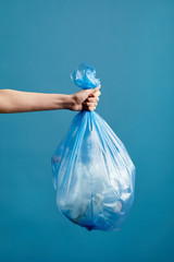 Vertical image of female hand holding trash bag with plastic against blue background, waste sorting...