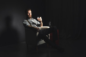 Portrait of a pensive handsome young man, with a glass of alcohol in his hands, on an isolated black background. The concept of pastime, rest and relaxation