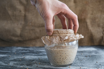 hand hold or puts glass jar with rye sourdough on table, yeast-free leaven starter for healthy organic rustic bread
