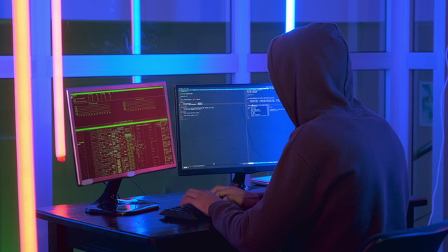 Medium shot of hacker dressed in a dark close working on computer. He penetrating network system. Back view