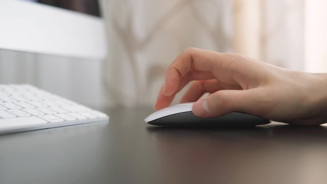 Woman works in the office at the computer and clicks on a white computer mouse