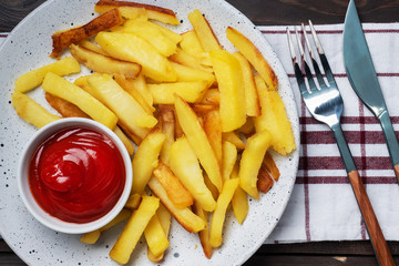 Fried French fries potatoes with tomato ketchup sauce on a plate. Wooden background. Copy space.