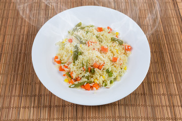 Rice boiled with vegetables on dish on bamboo table mat