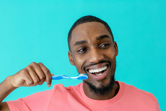 Portrait of a happy young man in pink shirt and great smile brushing teeth with toothbrush and looking to side, isolated on blue