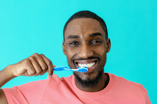 Portrait of a happy young man in pink shirt and great smile brushing teeth with toothbrush, isolated on blue