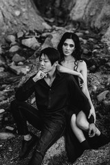 Asian couple in love hugs sitting on the rocks. Black-white