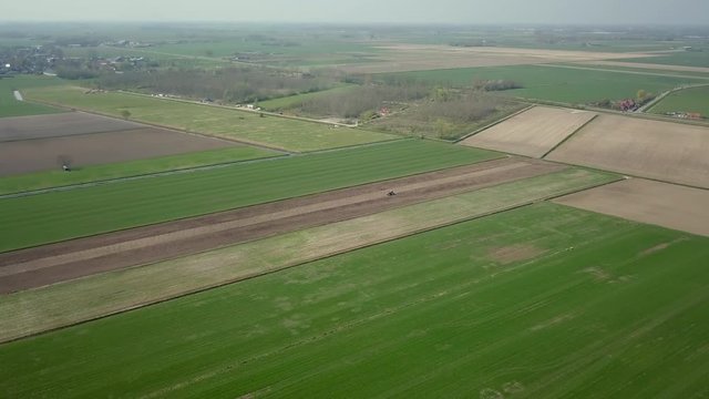 Aerial drone shot over the big wide farm fields with the tractor is moving to plow the ground