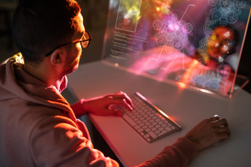 Over shoulder view of young engineer in glasses sitting at table and designing 3D model on computer