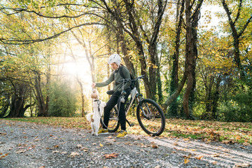 Naklejka premium 19/4/2020 Asian woman with a bike feeding a dog in autumn at the Botanic garden, Oamaru, New Zealand. Concept about exercise while social isolation from Coronavirus or Covid 19.