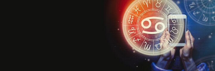 Female hands are holding a phone and an astrological circle with the zodiac sign Cancer against the background of the starry sky. Mobile Application for the horoscope. Banner. Copy space