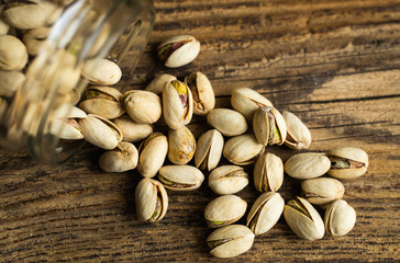 Pistachios scattered on the wooden vintage table from a jar. Pistachio is a healthy vegetarian protein nutritious food. Pistachios on rustic old wood.