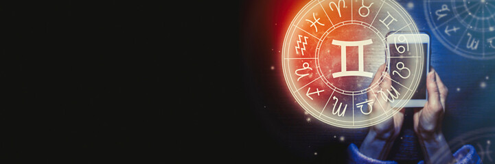 Female hands are holding a phone and an astrological circle with the zodiac sign Gemini against a starry sky. Mobile Application for the horoscope. Banner. Copy space