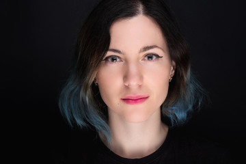 Portrait of a young caucasian woman with blue colored hair. Dark background, smiley face