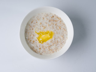 Oatmeal in milk with butter in a white round bowl on a light background. Top view